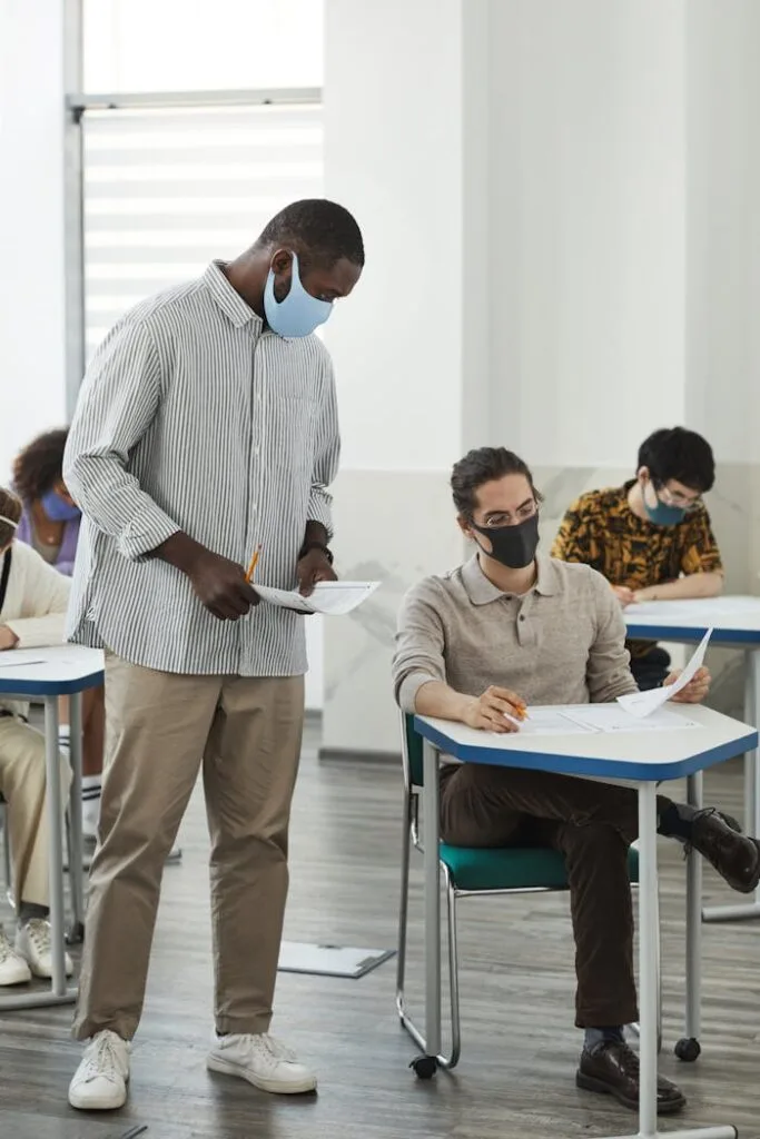 Students and teacher in masks during a classroom exam amid COVID-19 precautions.