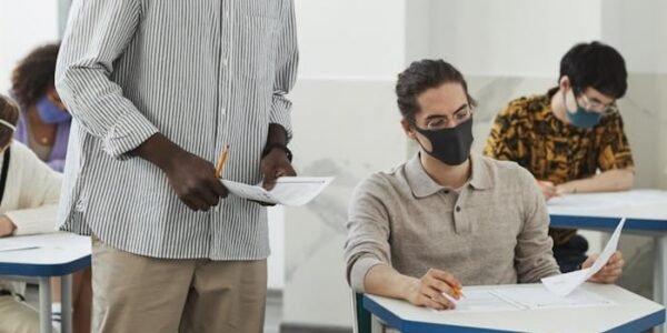 Students and teacher in masks during a classroom exam amid COVID-19 precautions.