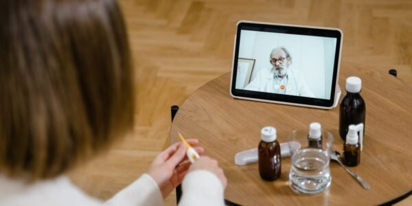 A doctor provides an online consultation via video call on a tablet, seen on a wooden table.